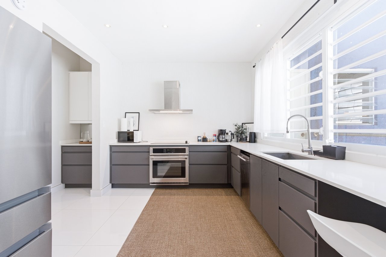 Modern kitchen with dark gray cabinets, white counters, and a large sink beneath wide windows.
