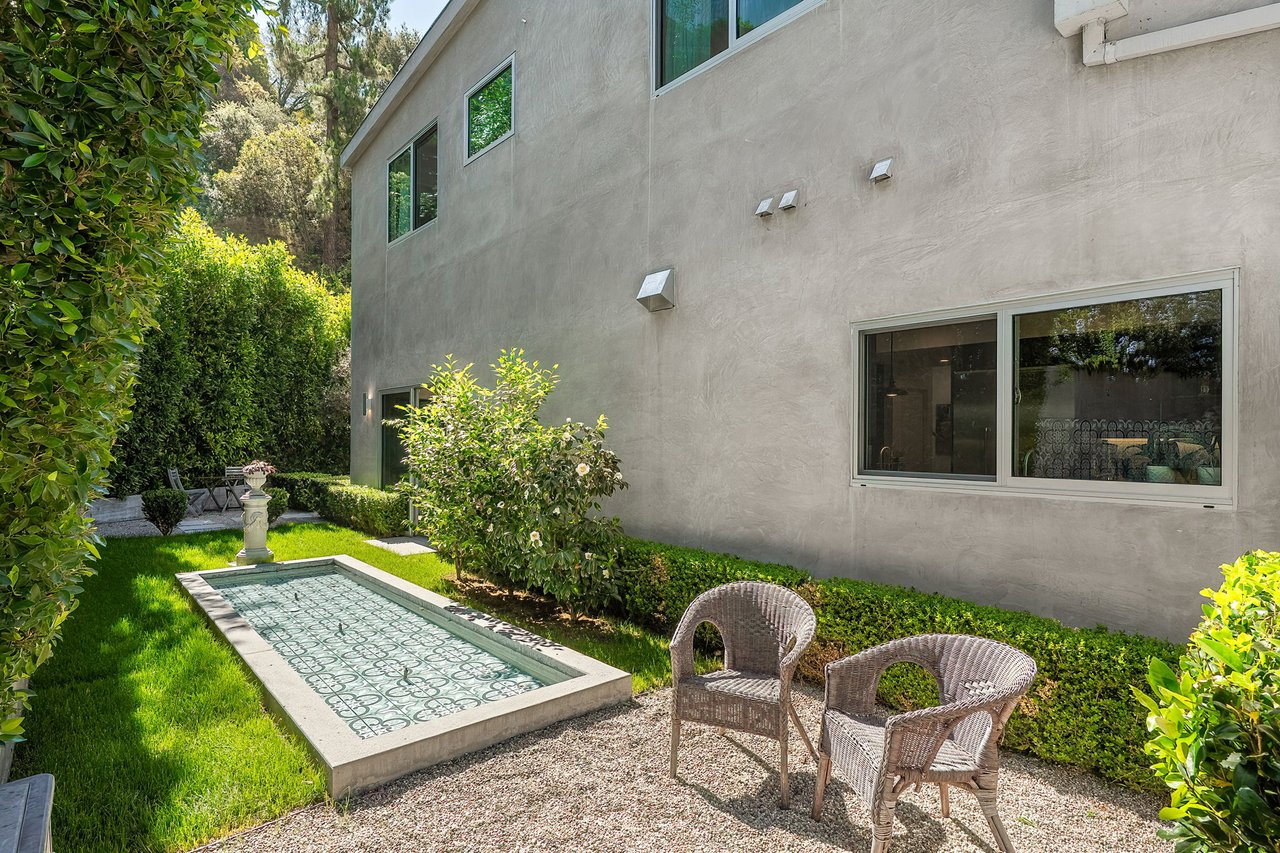 Courtyard pool beside a modern stucco home, with wicker chairs on a gravel patio.