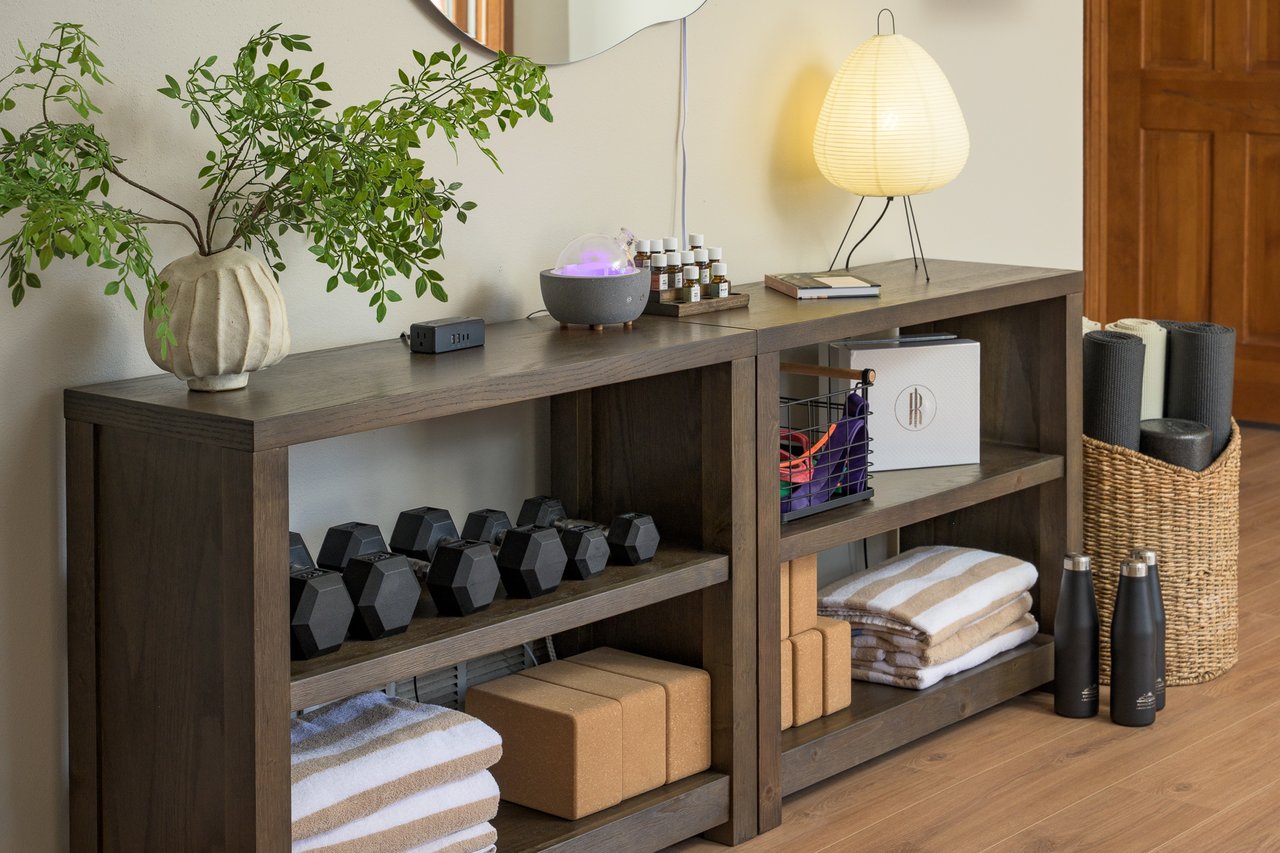 Home wellness area with dumbbells, folded towels, yoga blocks, and a leafy plant on a dark wood console.