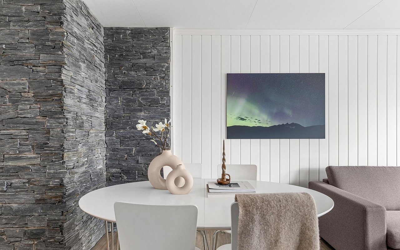 Dining area with a white oval table, dark stone accent wall, and framed aurora print.