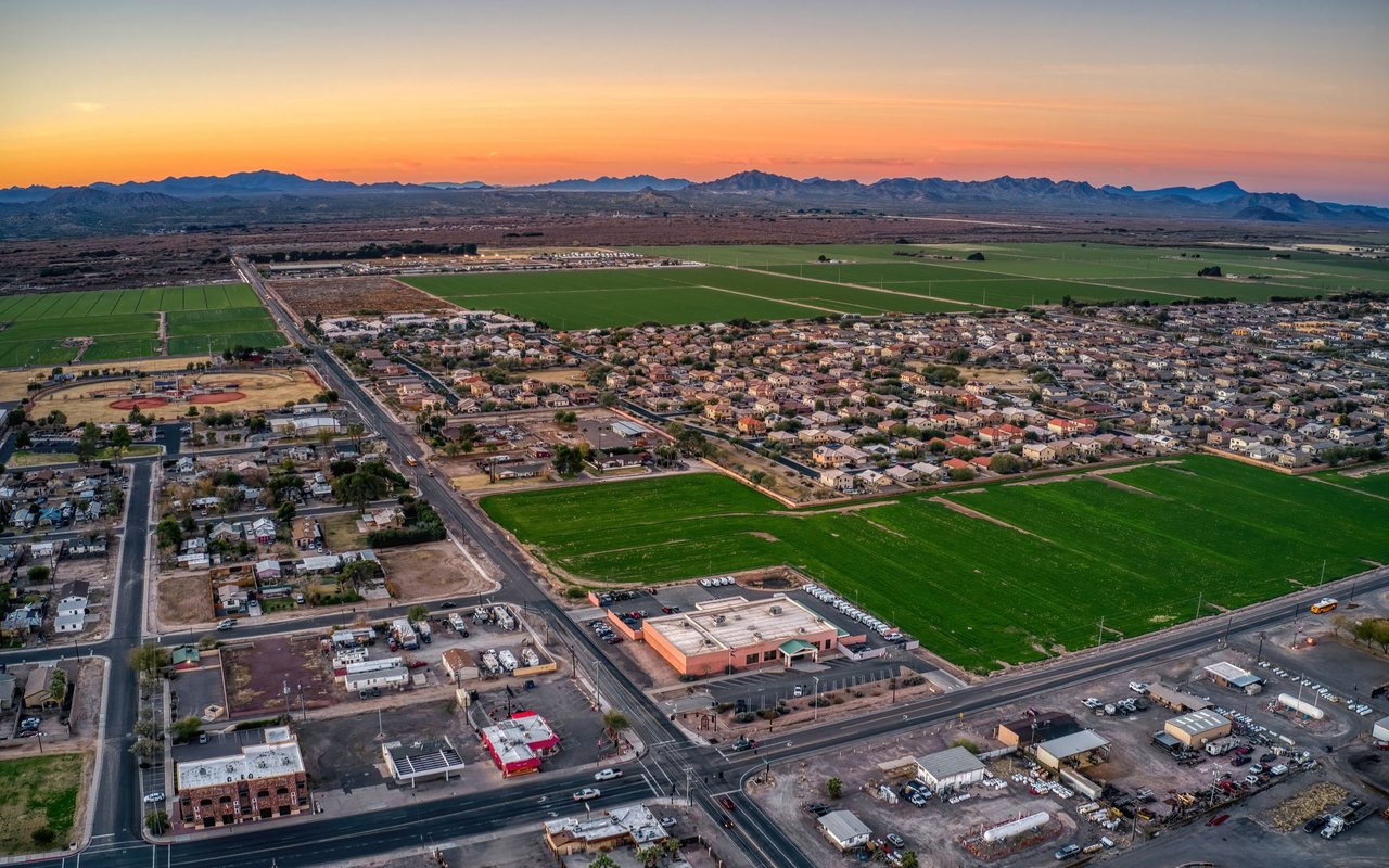 Aerial view of a suburban community and green fields with mountains on the horizon at sunset.