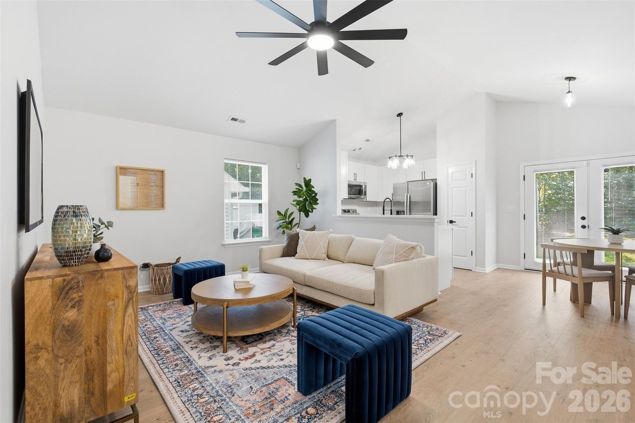 Open-plan living room with cream sofa, blue ottomans, patterned rug, and adjoining white kitchen.