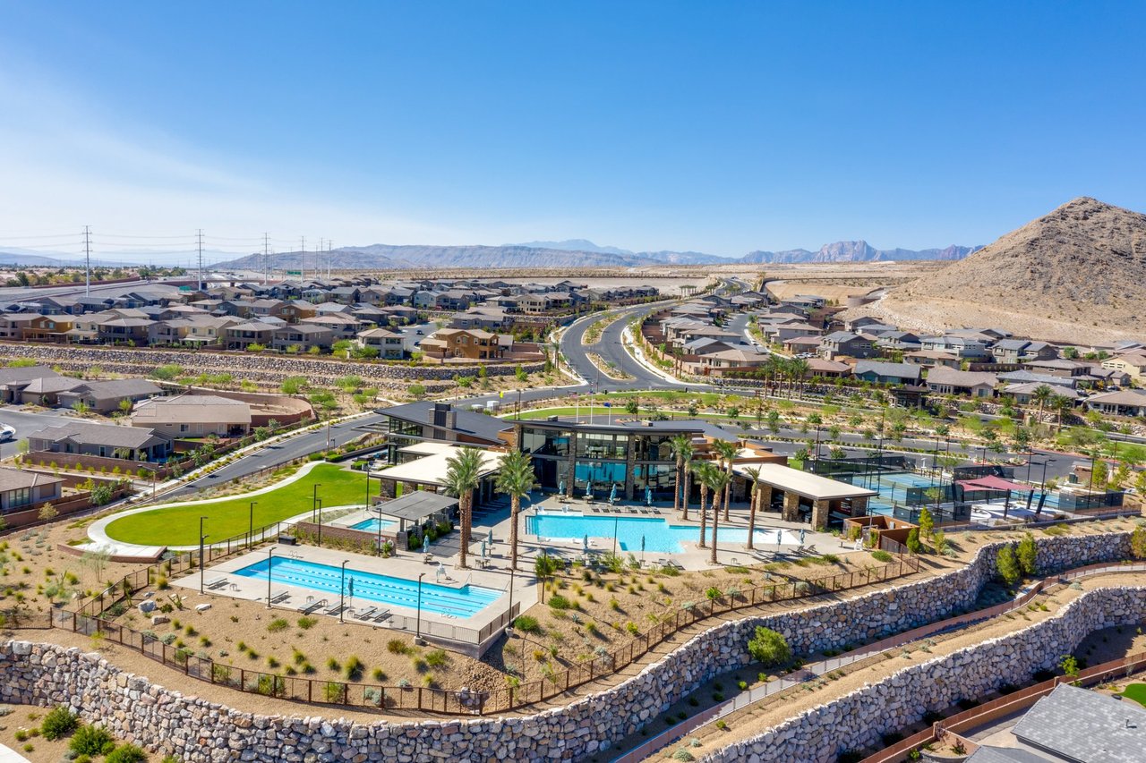Aerial view of The Clubhouse at Reverence in Summerlin, with its resort pool, lap pool, event lawn and courts set among guard-gated homes and desert mountains.