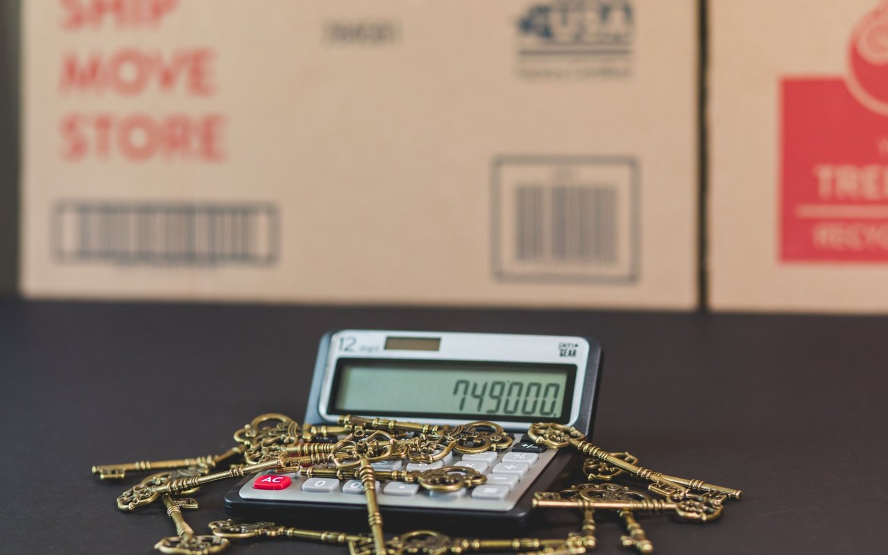 Calculator displaying 749000 among ornate brass keys, with moving boxes in the background.