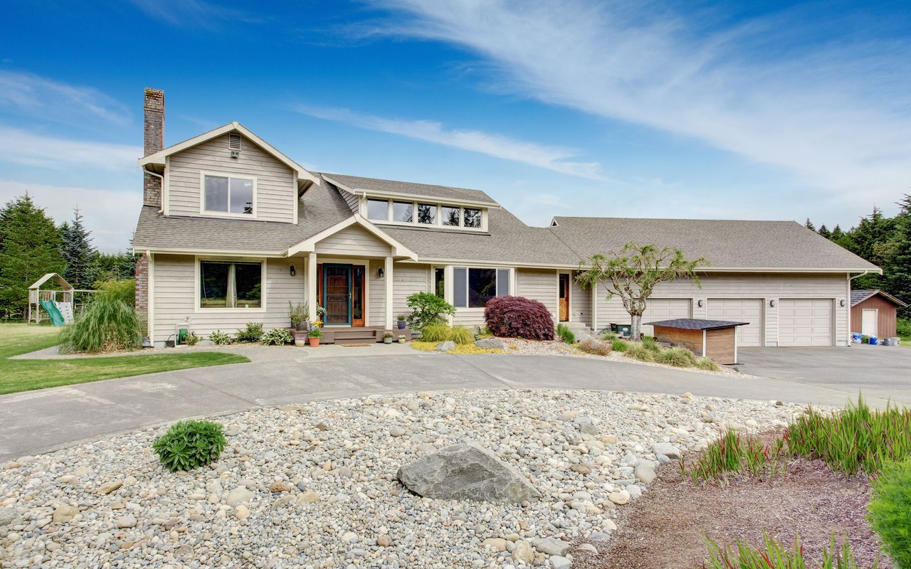 Beige two-story house with a three-car garage, brick chimney, and landscaped front yard.