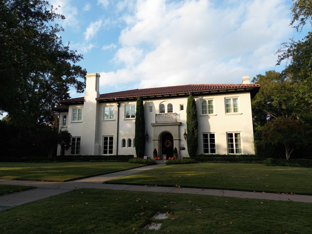 White stucco home with a red tile roof, arched entry, small balcony, and expansive front lawn.