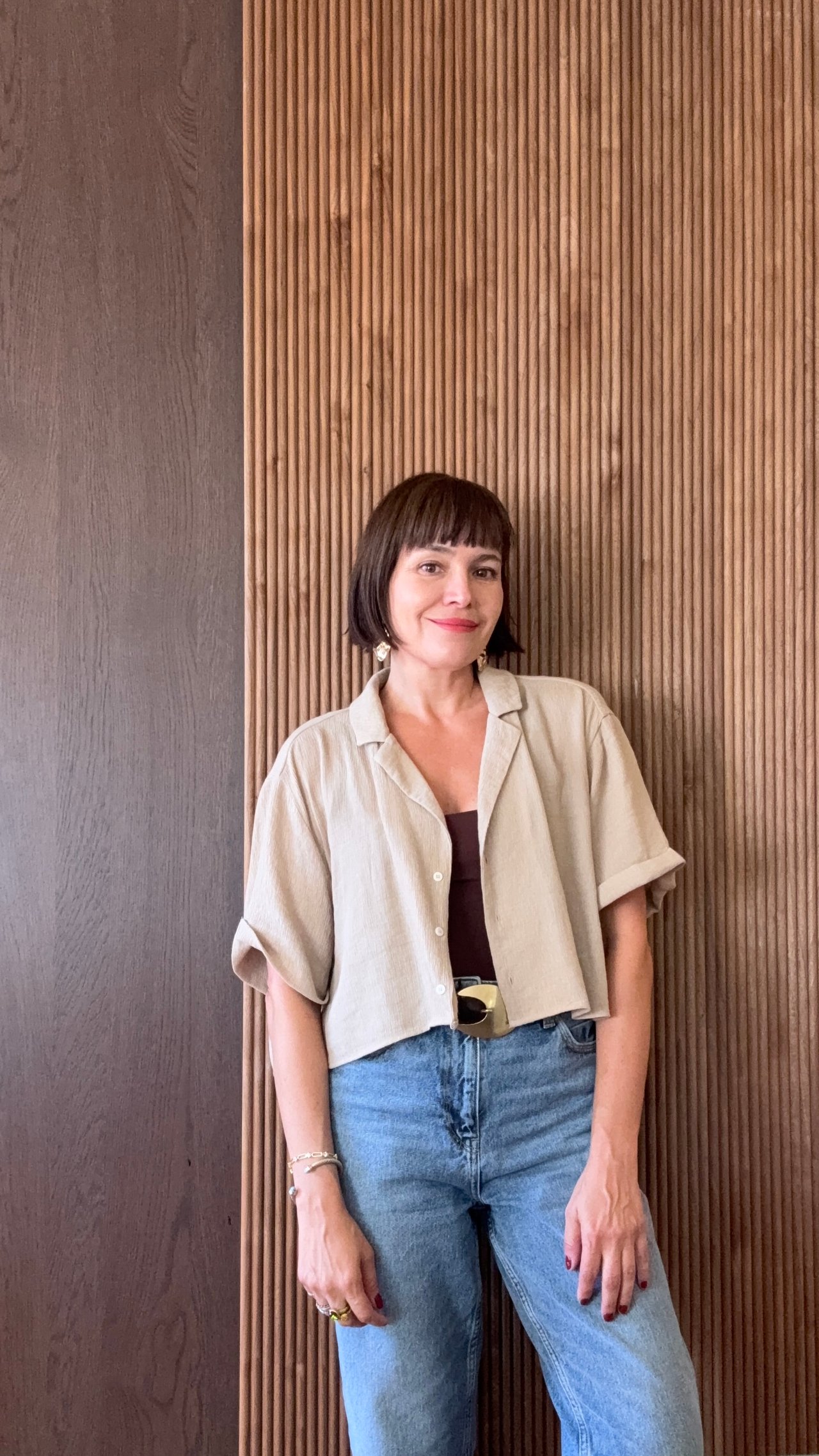 Lorien Olsen poses in a beige shirt and jeans against a wood-slat wall.