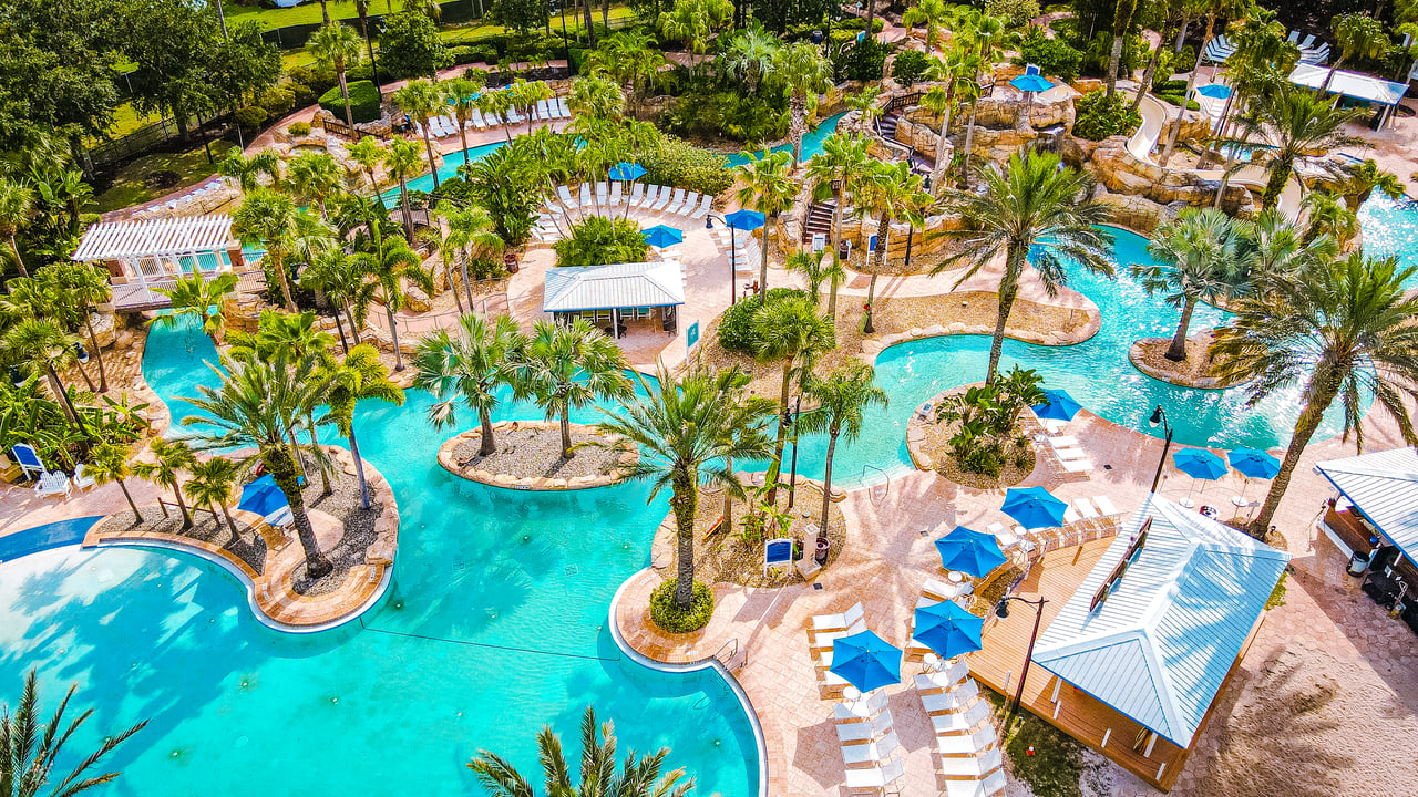 Aerial view of Reunion’s winding resort pools, palm-planted islands, and blue umbrellas.