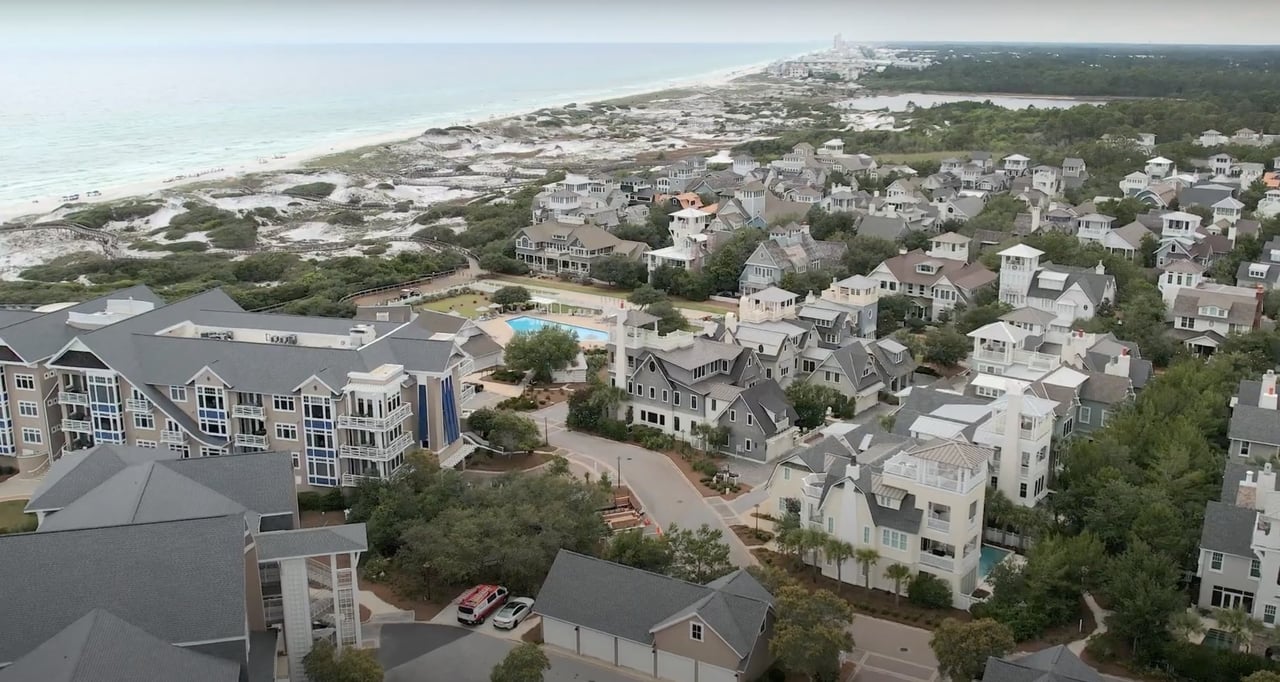 Aerial coastal neighborhood with clustered homes and a community pool beside the shoreline.
