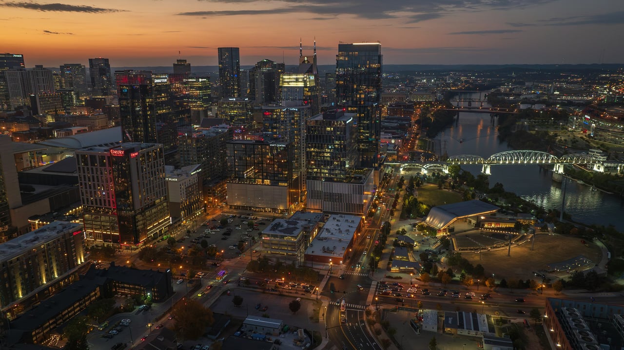 Downtown Nashville skyline at dusk, with the Cumberland River and an illuminated bridge.