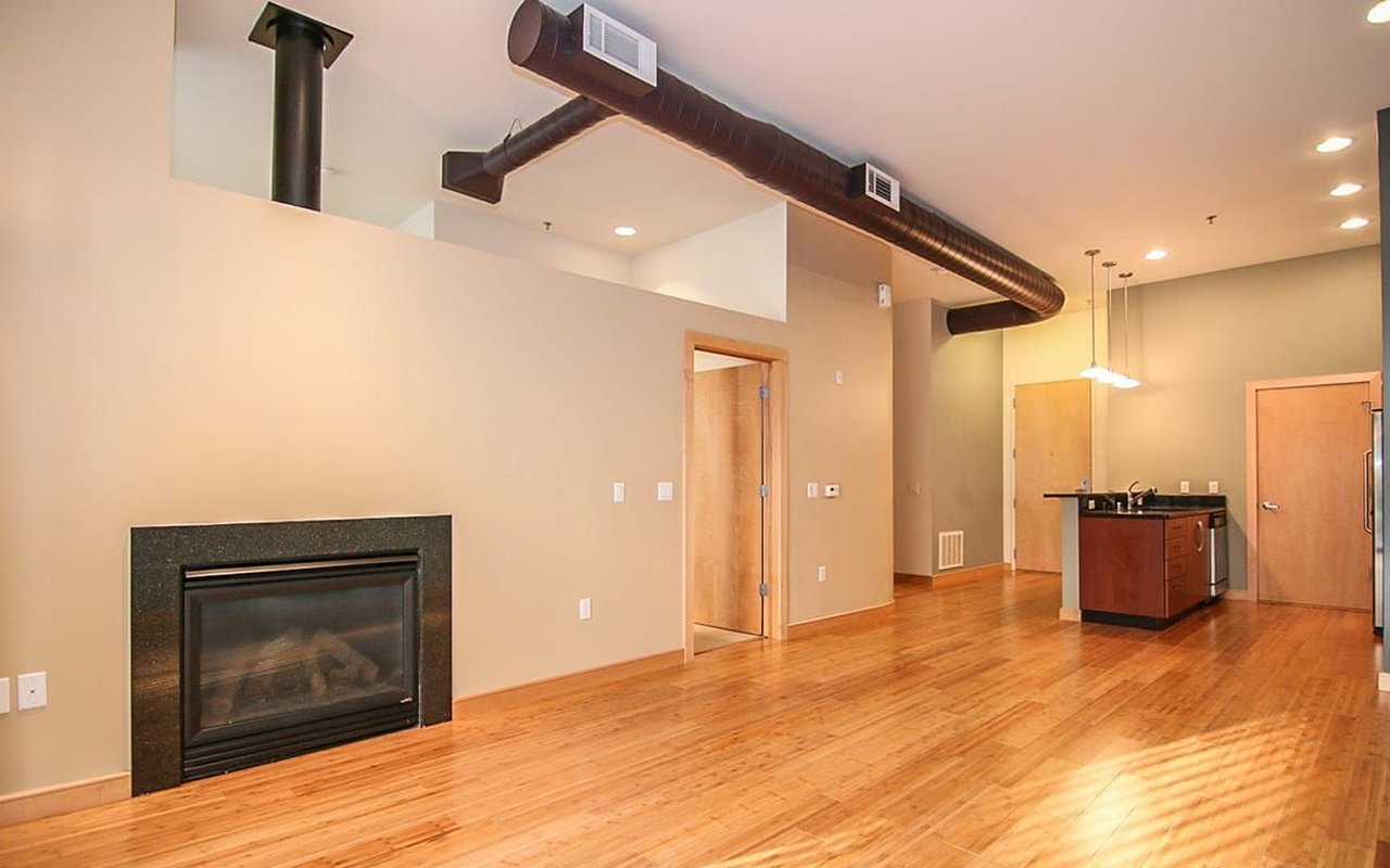 Open loft living area with hardwood floors, a fireplace, exposed ductwork, and a kitchen island.