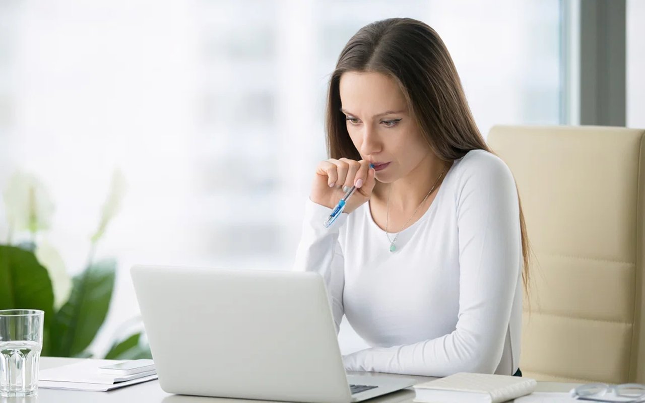 Woman thoughtfully looking at a laptop with a pen in hand