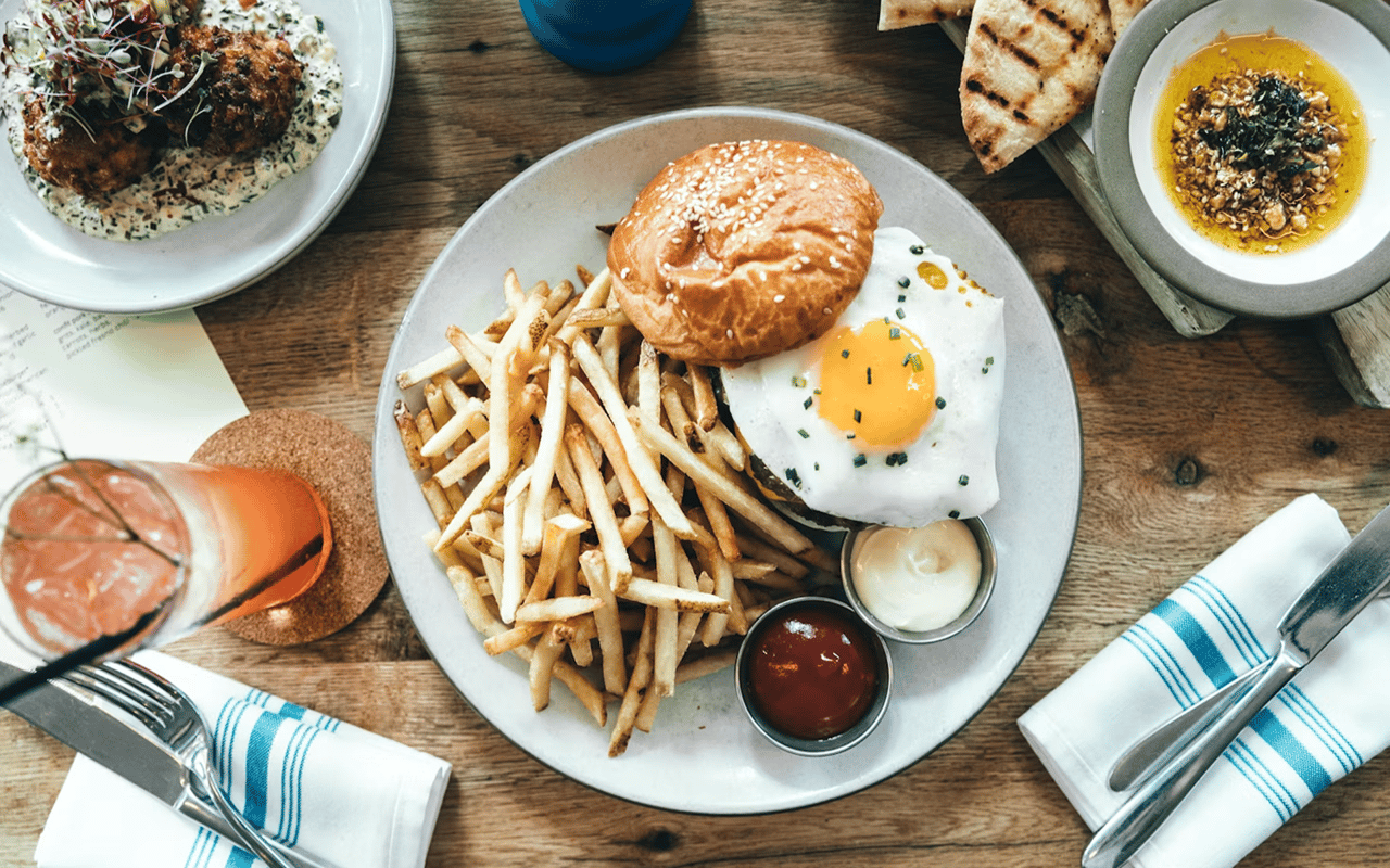 Fries, fried egg, and sesame bun with ketchup and mayonnaise on a restaurant table.