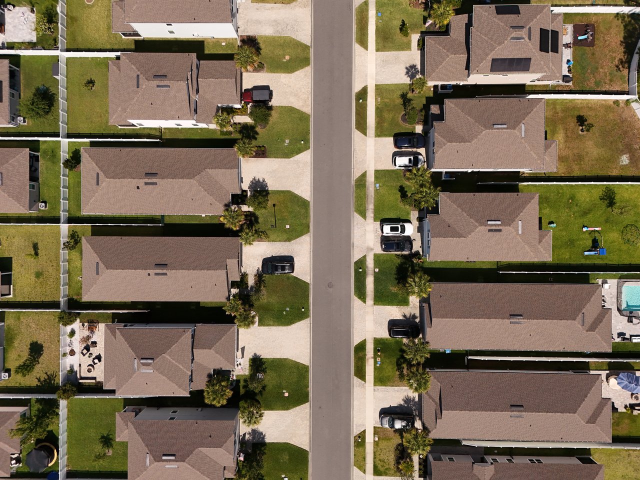 Aerial view of detached homes along a residential street, with fenced yards and parked cars.