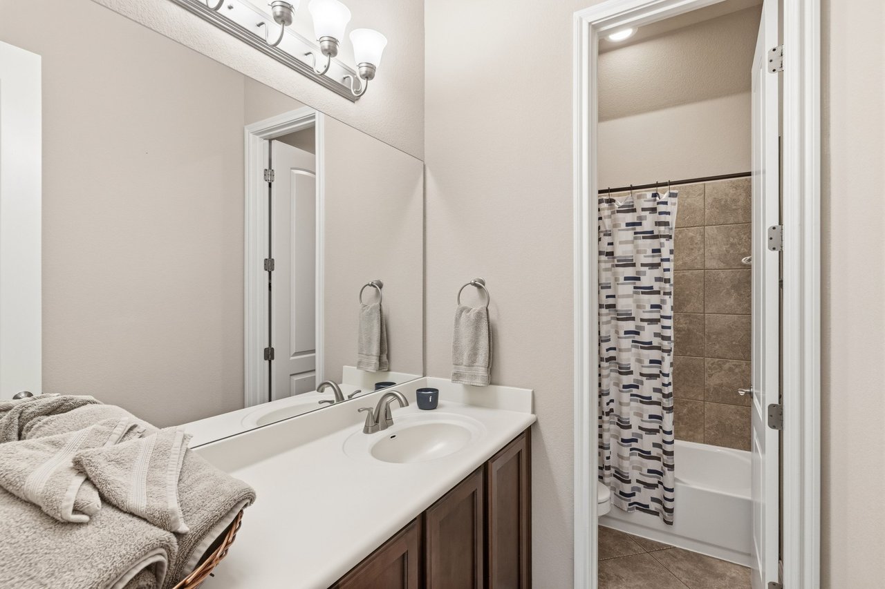 Bathroom with a double-sink vanity and tiled tub behind a patterned shower curtain.