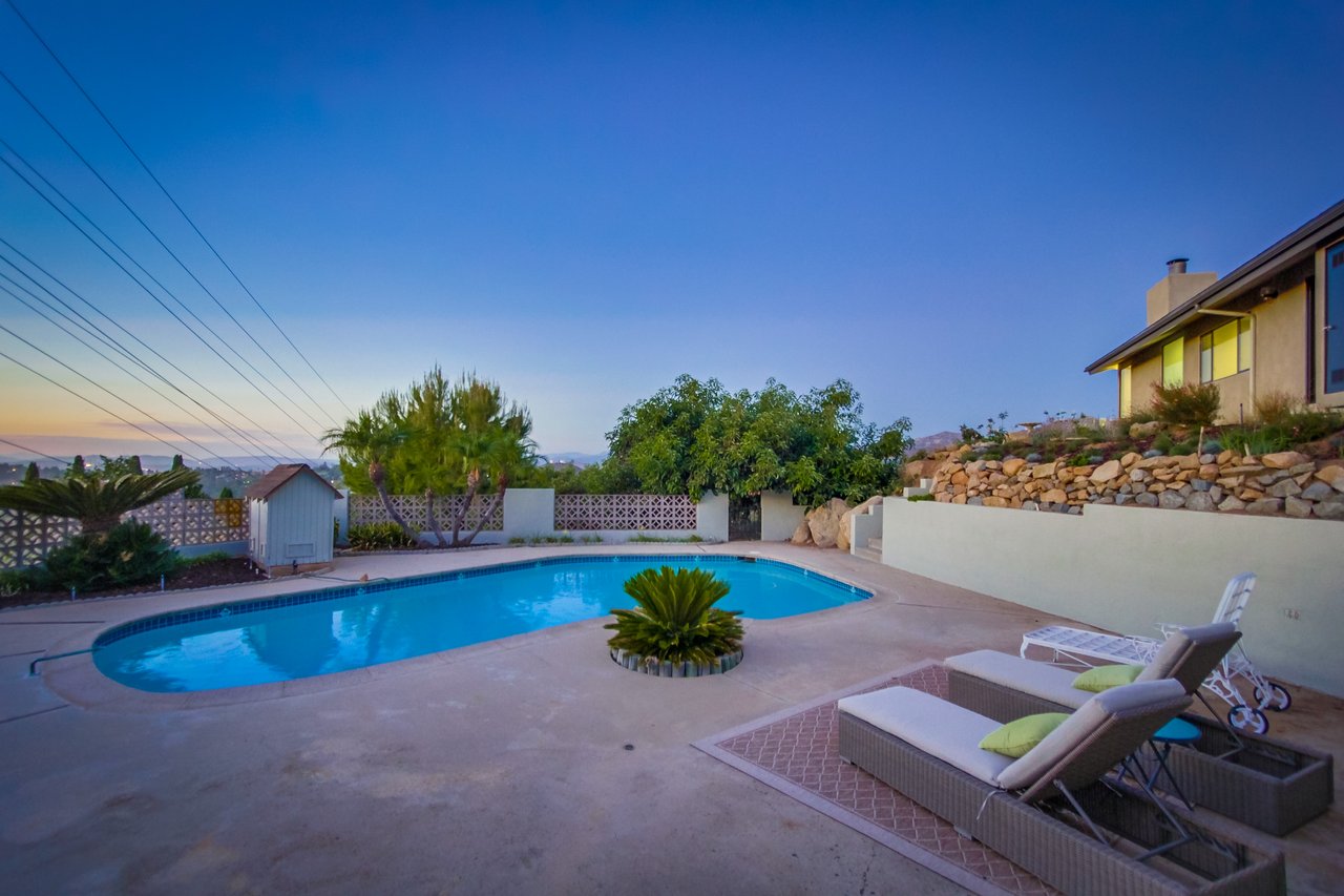 Backyard pool and patio at dusk, with outdoor loungers and a raised rock garden.