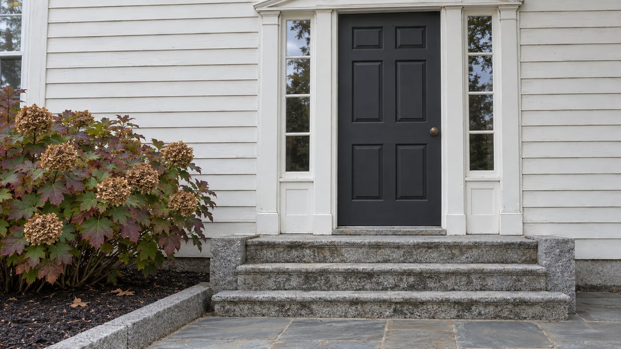 Traditional clapboard entry with a charcoal paneled door, paired sidelights, granite steps and autumn oakleaf hydrangea.