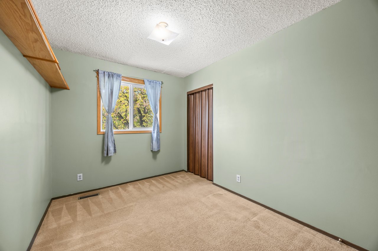 Empty bedroom with pale green walls, beige carpet, blue curtains, and a sliding wooden closet door.
