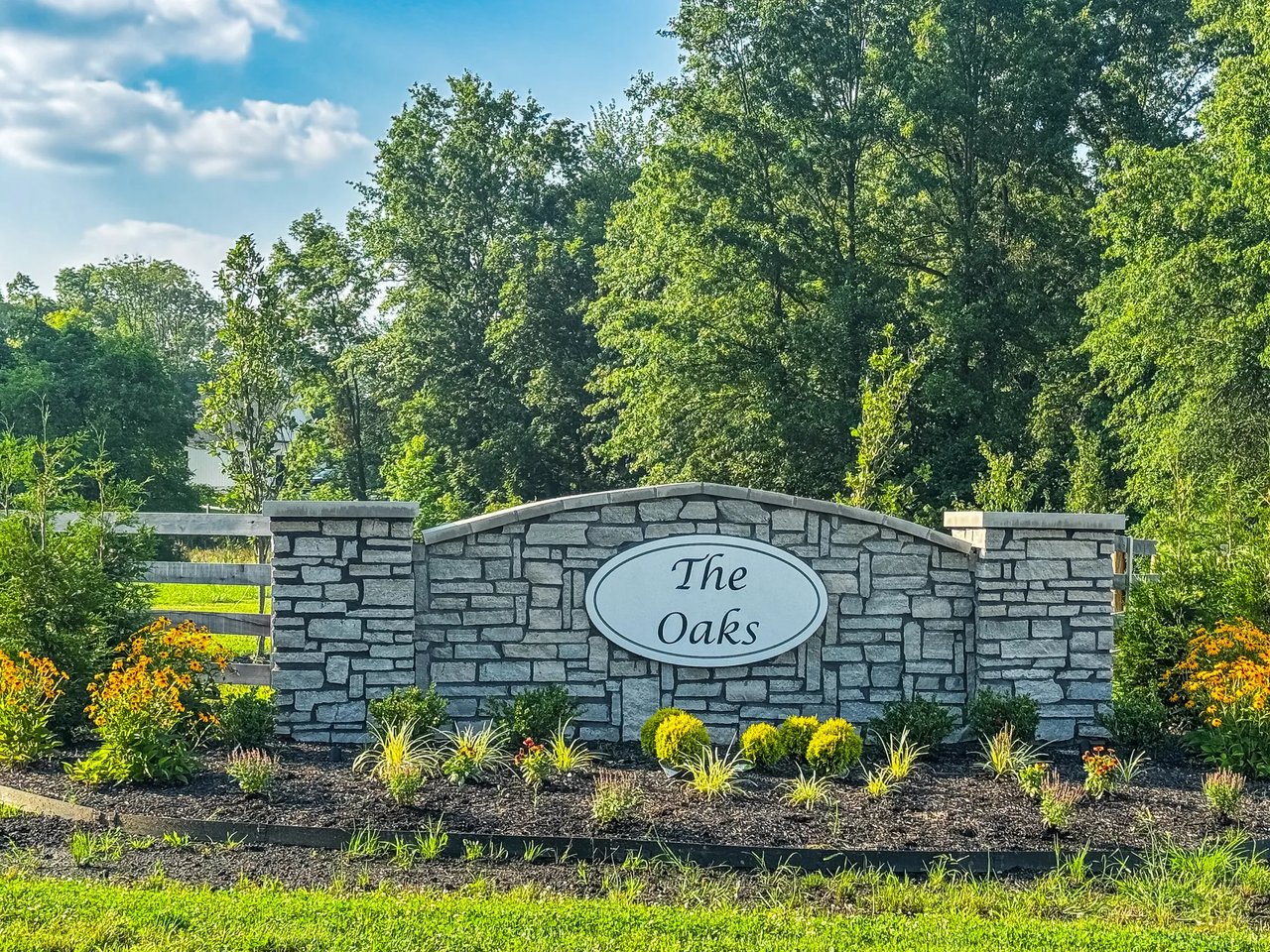 The Oaks at Big Walnut stone entrance monument in Sunbury Ohio with summer landscaping and mature tree canopy, an exclusive 14-lot estate community in Big Walnut Local School District