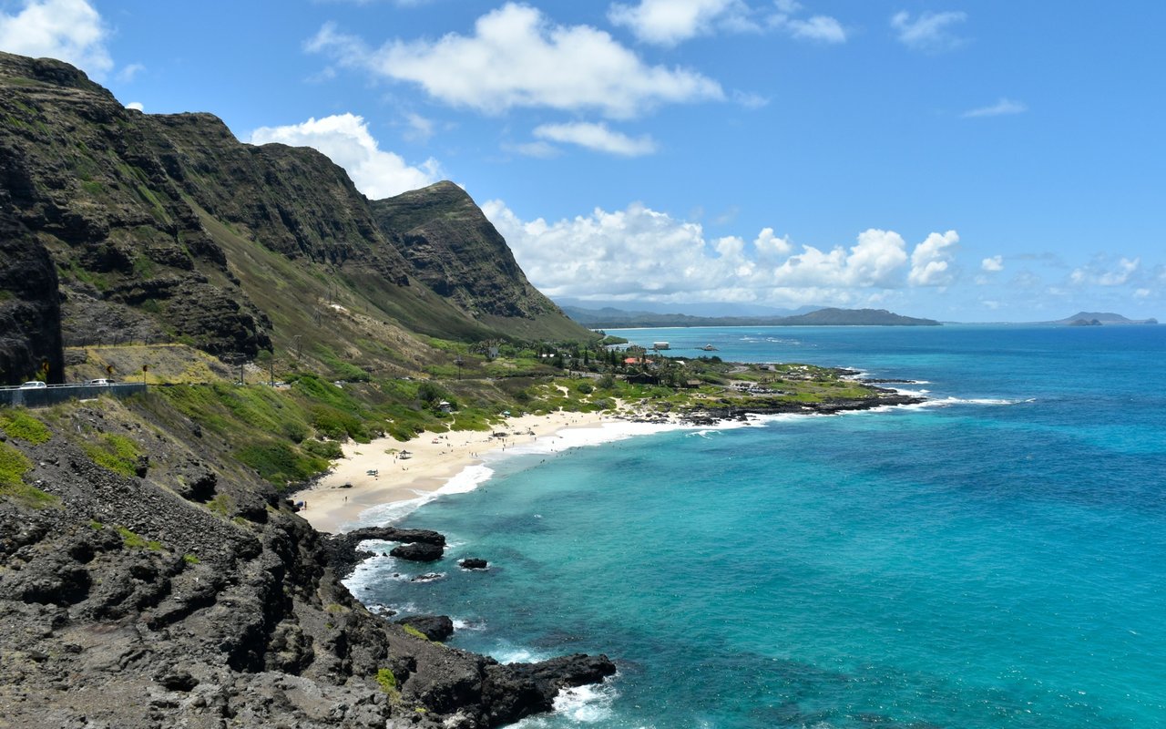 Rugged coastal cliffs overlook a sandy beach and turquoise ocean.