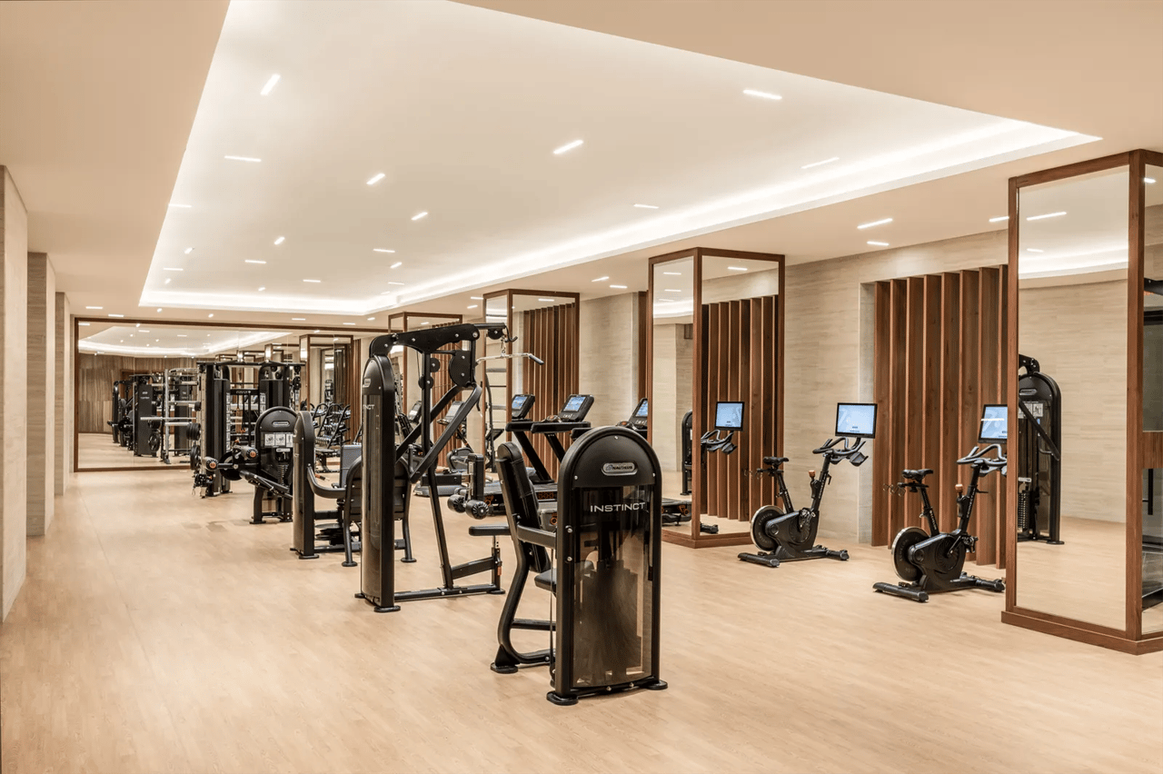 Gym with weight machines and exercise bikes, framed mirrors, and wood-slat partitions.