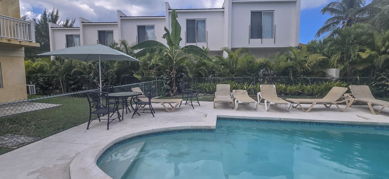 Outdoor pool beside a modern white residence, with sun loungers and tropical landscaping.