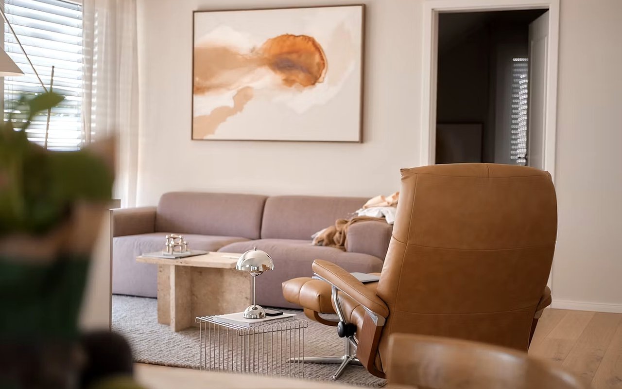 Living room with a caramel leather lounge chair facing a mauve sofa beneath abstract artwork.