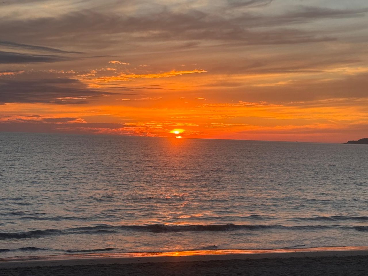 Ocean at sunset, with orange clouds, gentle waves, and a sandy shoreline.