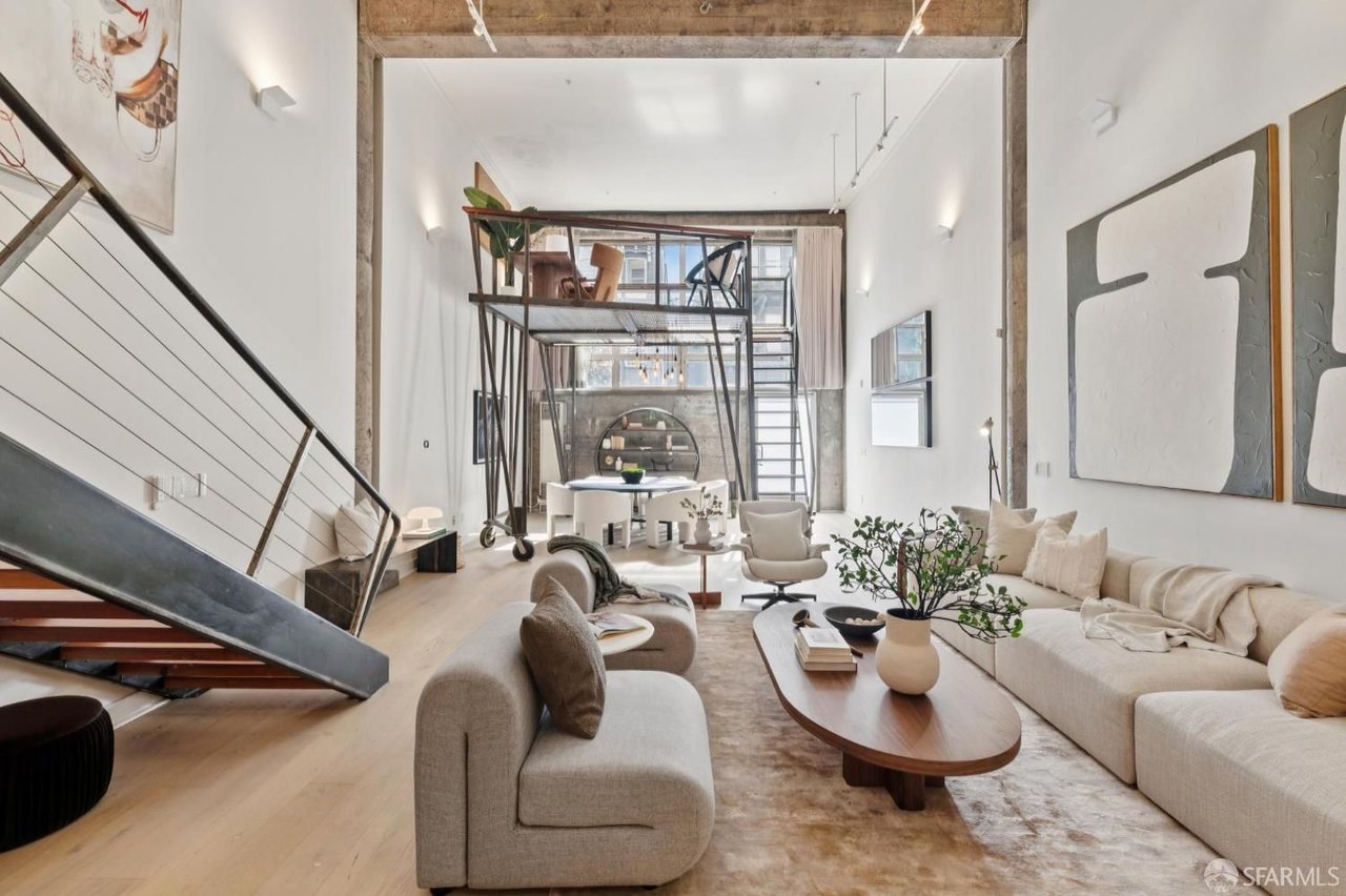 Loft living room with exposed beams, a metal staircase, and a raised mezzanine dining area.