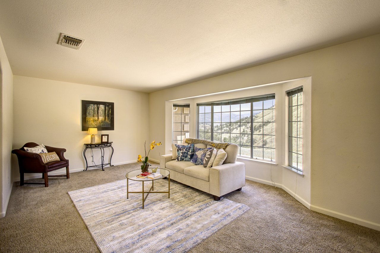 Staged living room with a cream sofa and large windows overlooking rolling hills.