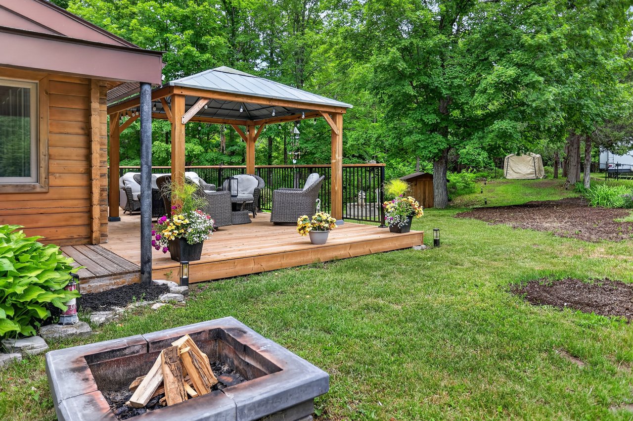 Cottage backyard with a furnished gazebo deck and a stone fire pit in the foreground.