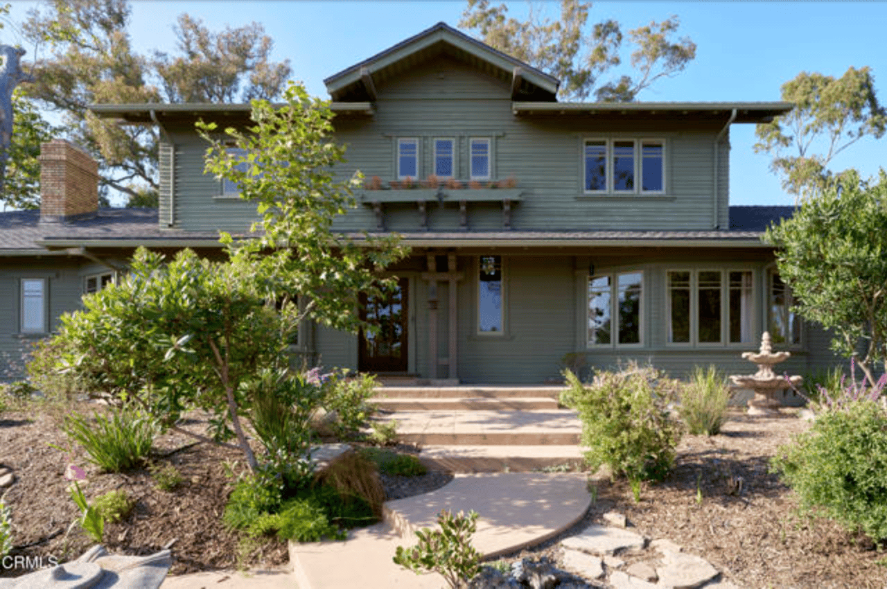 Two-story gray-green house with a central gable, landscaped entrance, and curved walkway.