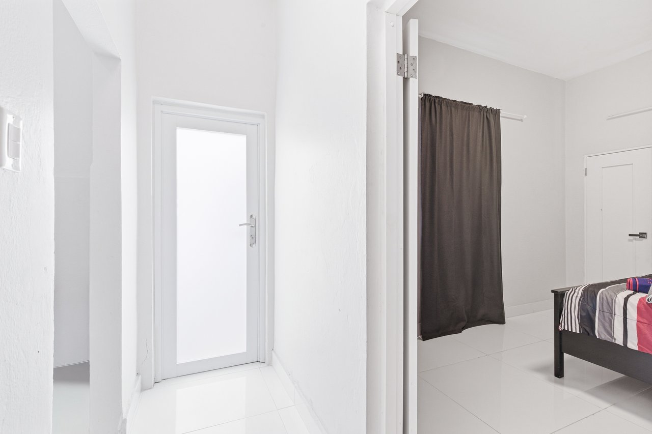 White tiled hallway opens into a bedroom with a dark curtain and partially visible bed.