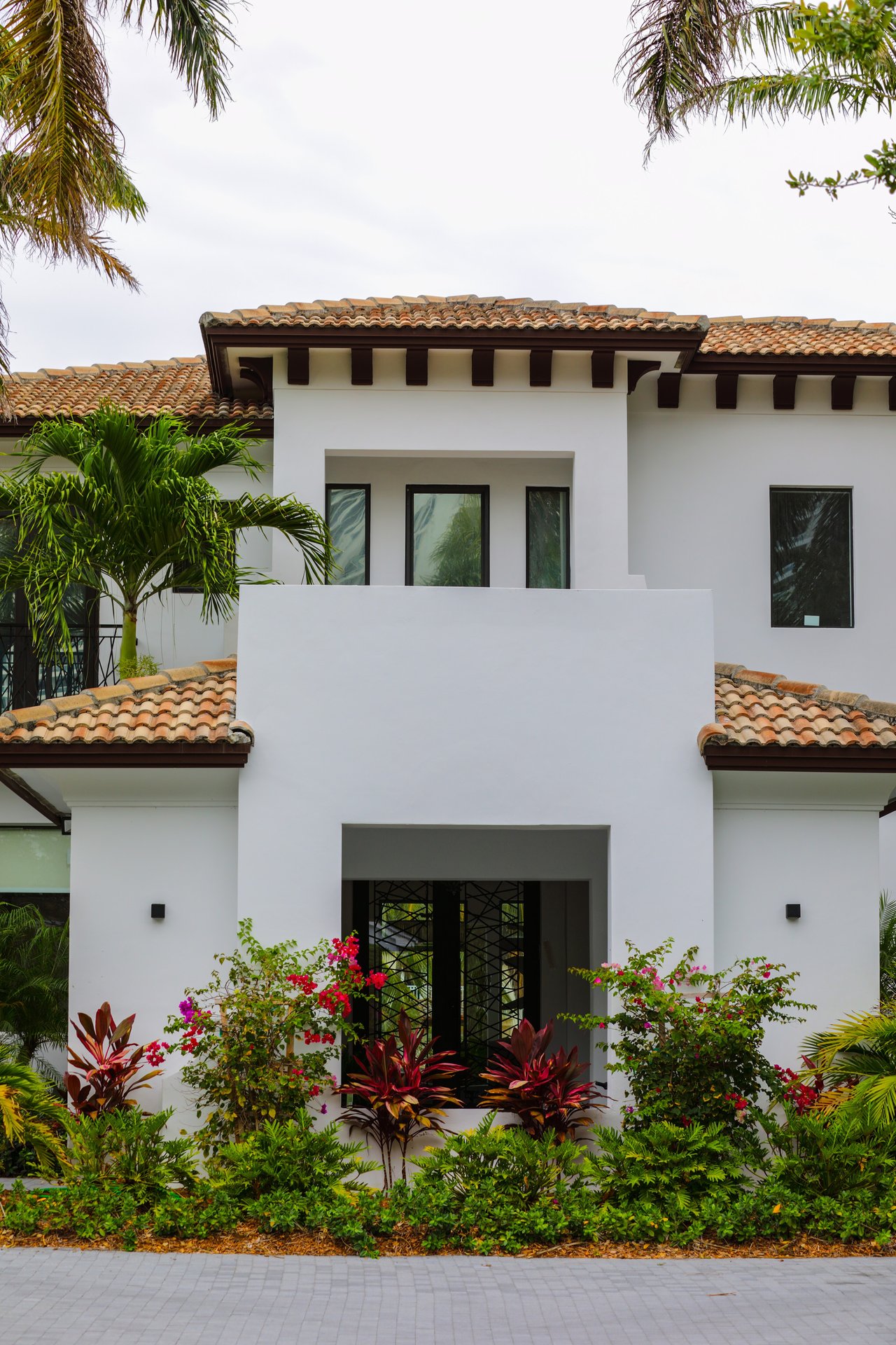 White stucco home with a terracotta tile roof, recessed entry, and tropical landscaping.