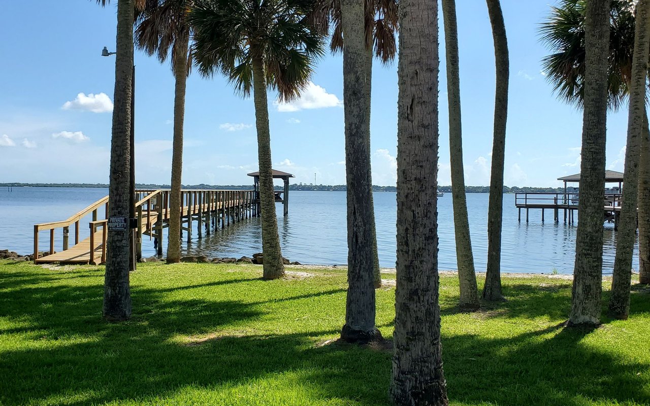Palm-lined Merritt Island waterfront with grassy shore and wooden piers over calm water.