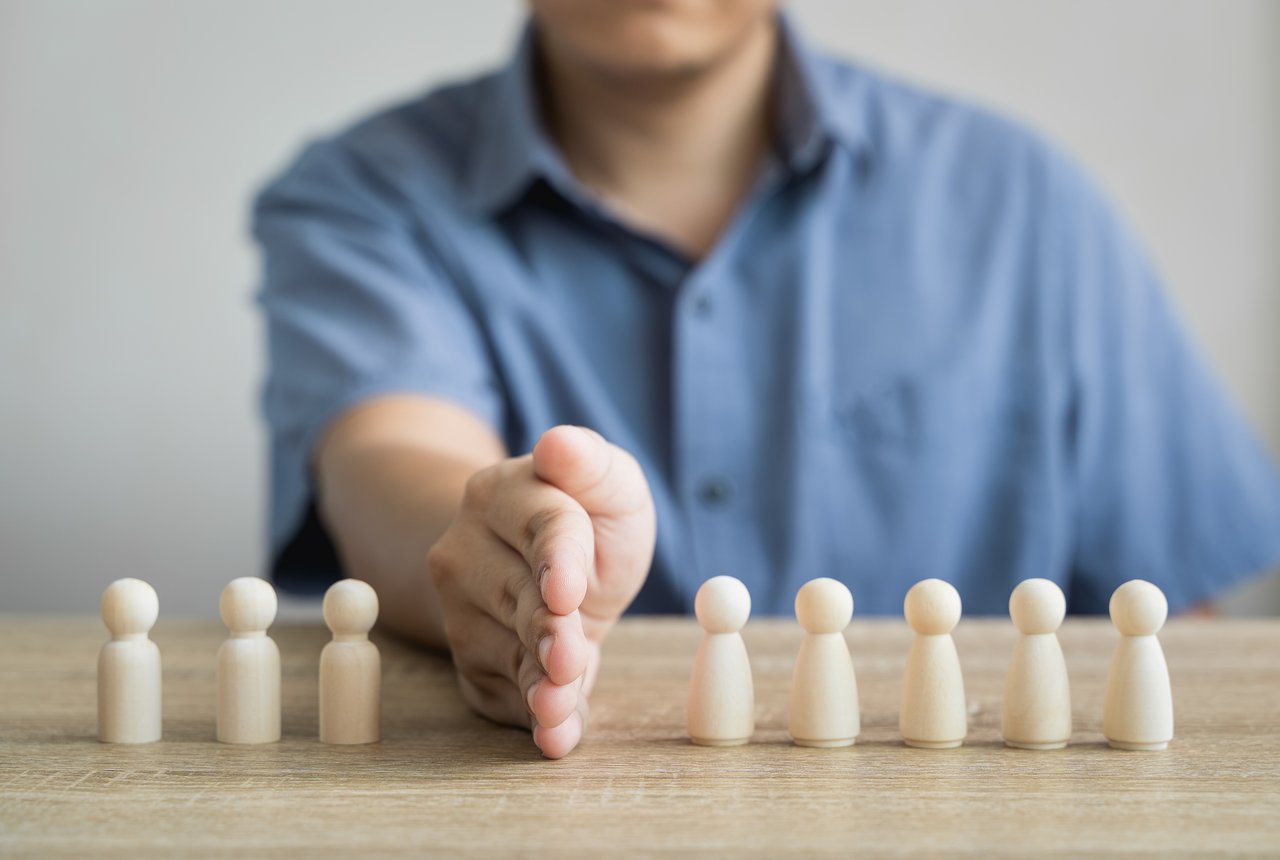 A hand separates two groups of wooden figures on a table.