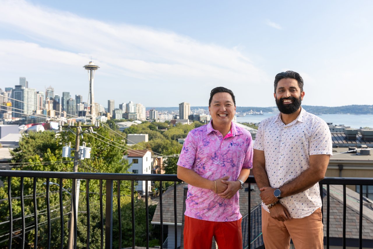 Two smiling men on a rooftop terrace with Seattle’s skyline and the Space Needle behind them.