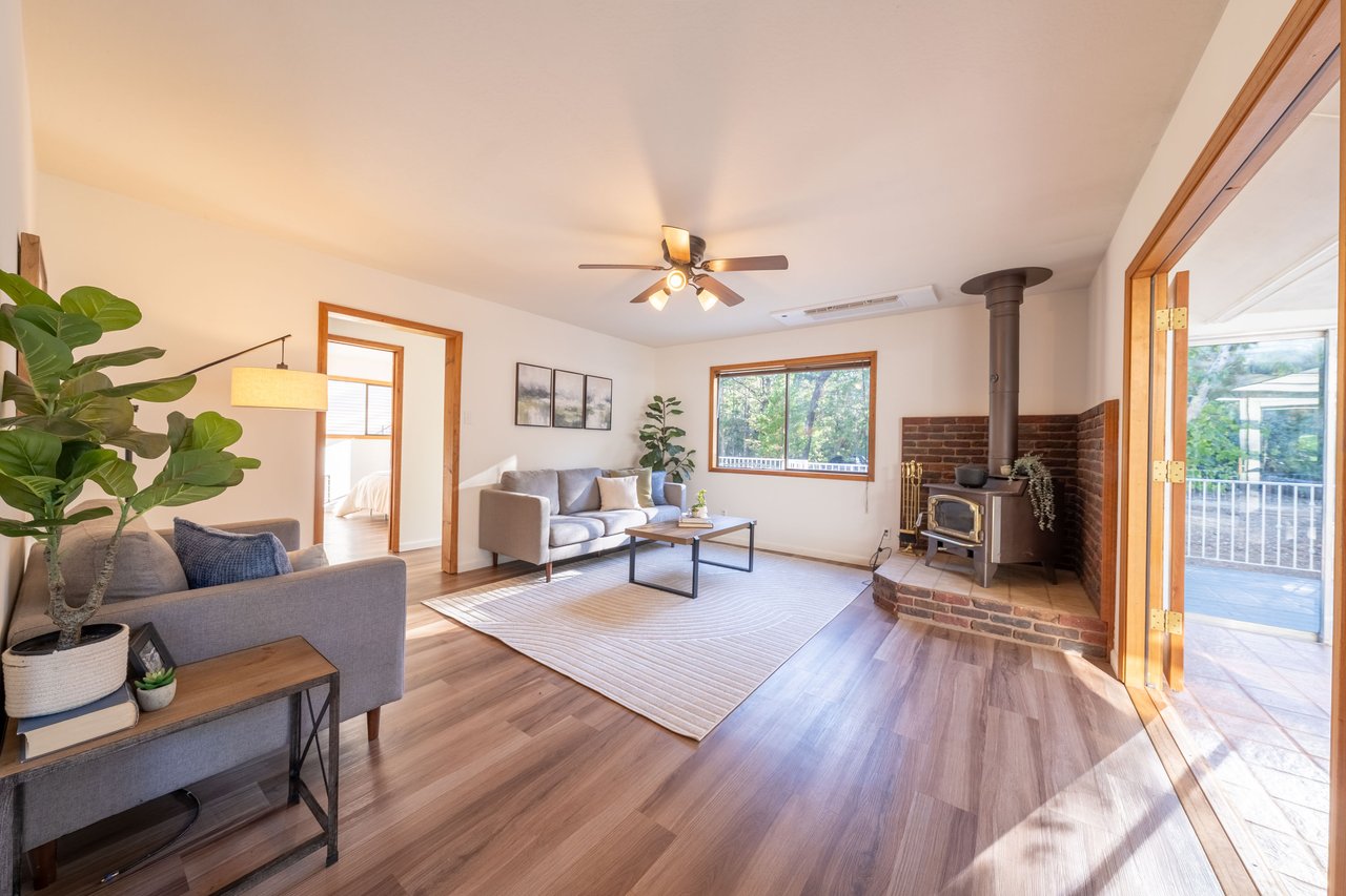 Living room with gray sofas, wood floors, and a brick-surround wood stove beside doors to a deck.