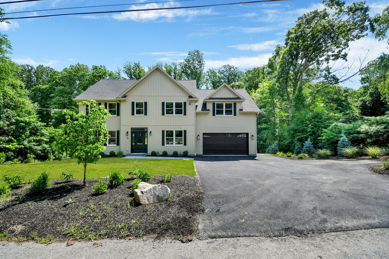 Two-story light-colored home with dark shutters, a black garage door, and a landscaped yard.
