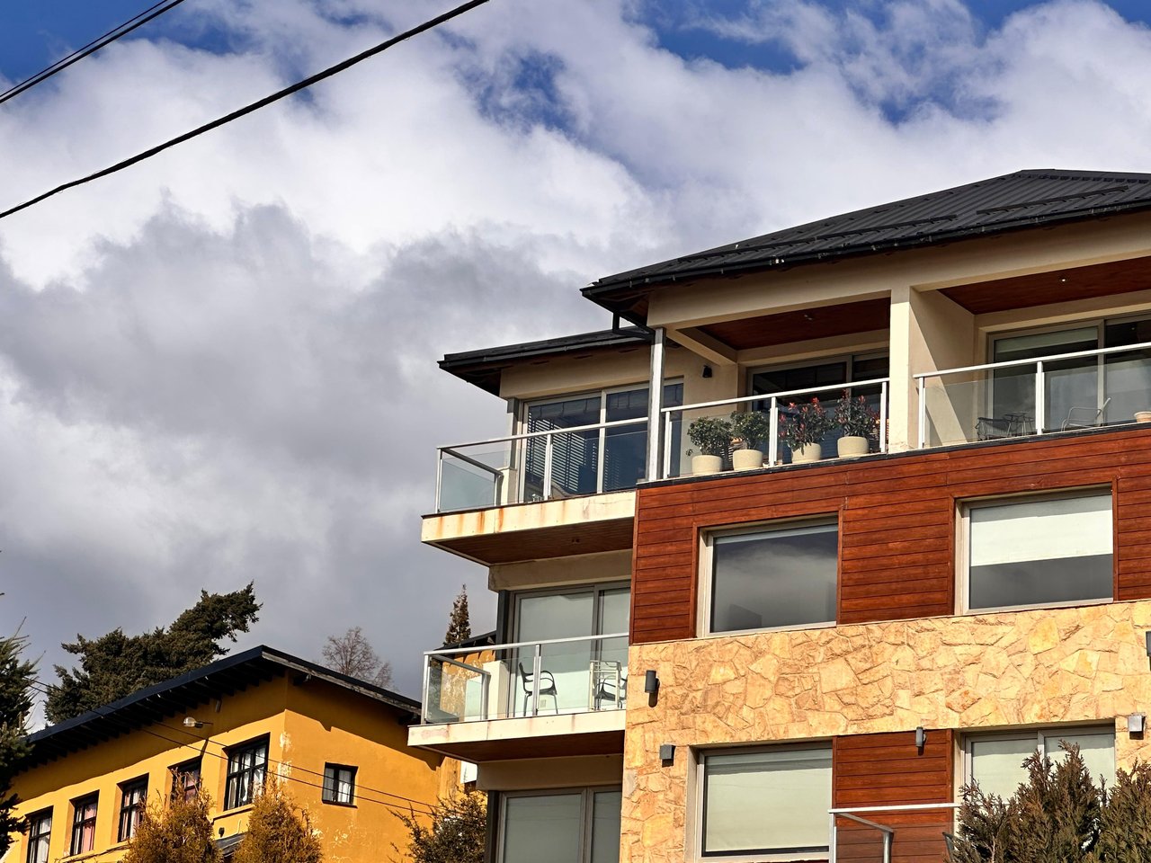 Modern apartment building with glass balconies, reddish wood siding, and stone cladding.
