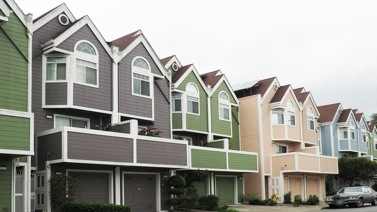 Row of colorful two-story townhomes with attached garages along a curving residential street