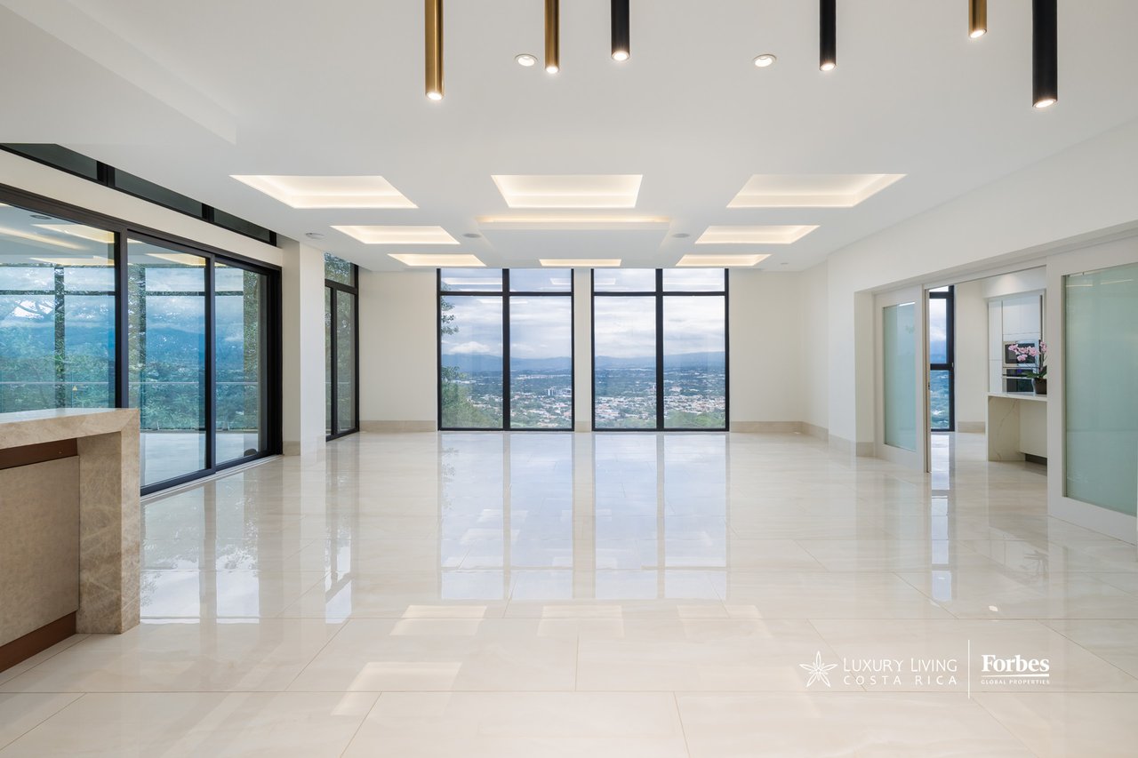 Empty luxury living area with floor-to-ceiling windows overlooking the city and mountains.