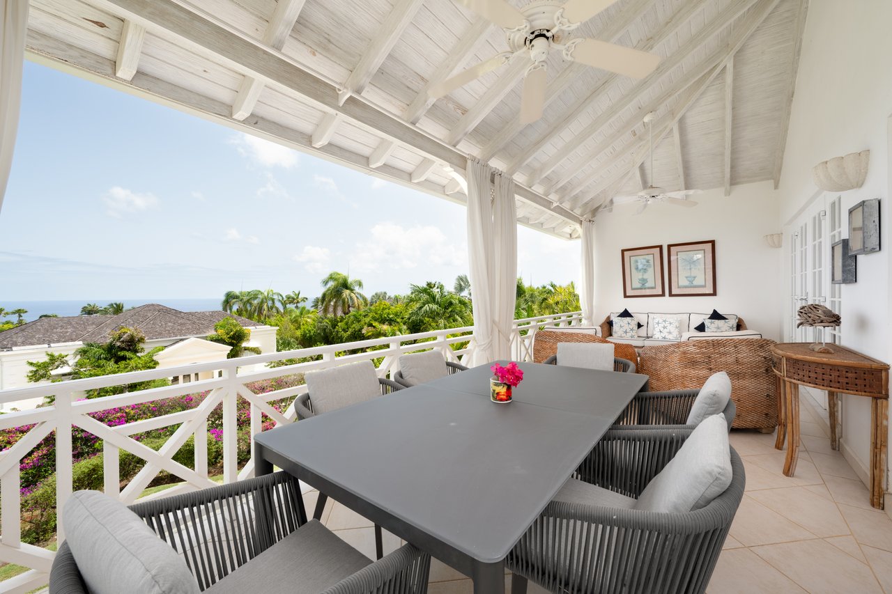 Covered terrace with outdoor dining and wicker seating overlooking tropical gardens and the ocean.