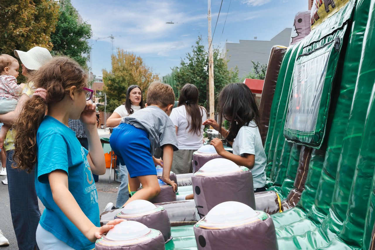 Children play at a neighborhood block party inflatable game as adults gather nearby.