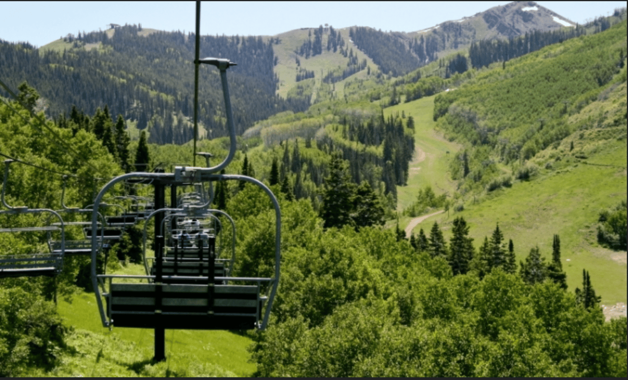 Winter scene of Town Lift Plaza in Park City, Utah, featuring the ski lift base, Main Street-style historic buildings, a pedestrian bridge, snow-covered mountains, and skiers in seasonal gear—capturing the charm and vibrancy of Park City’s resort core.