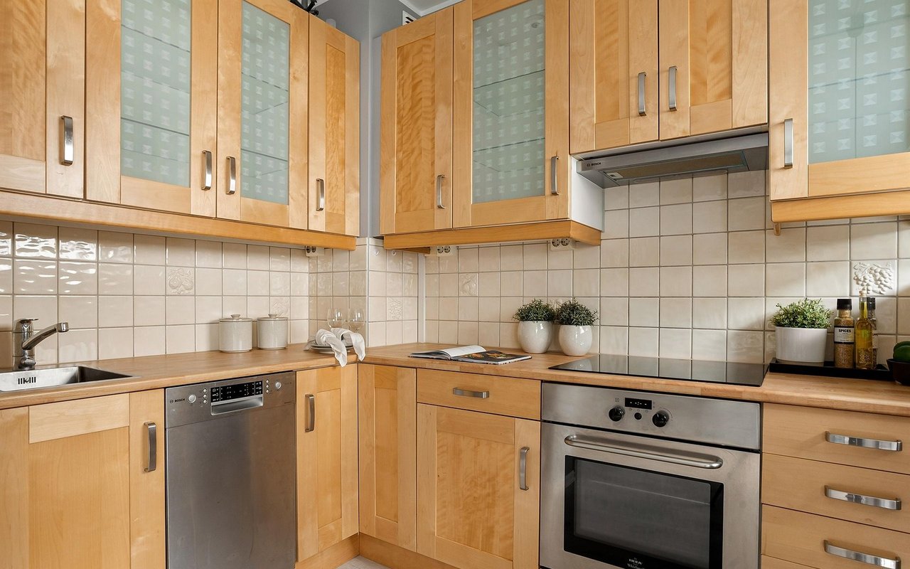 Kitchen with honey-colored wood cabinets, frosted glass doors, tiled backsplash, and stainless steel appliances.