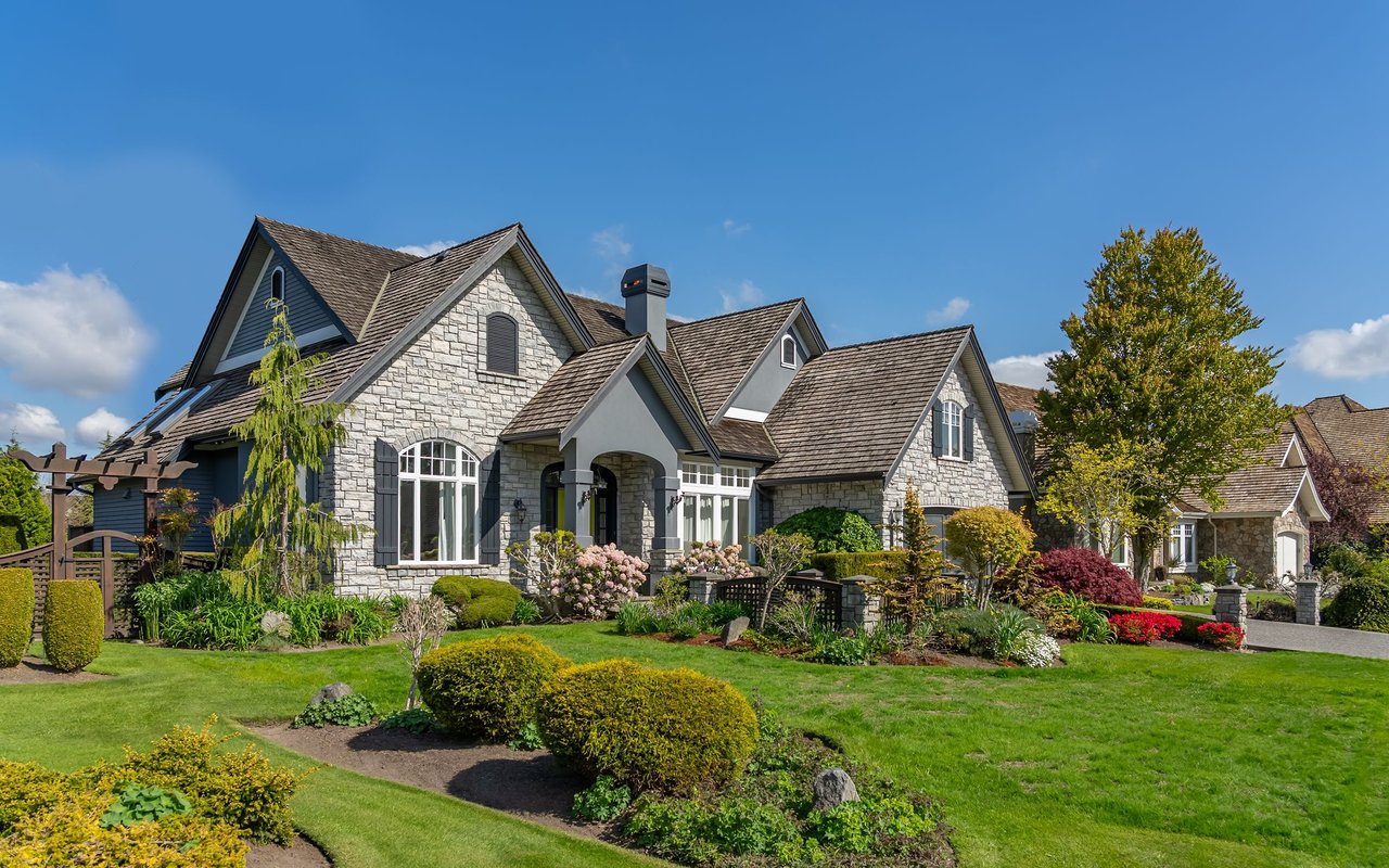 Gray stone home with multiple gables, a covered entry, and manicured gardens.