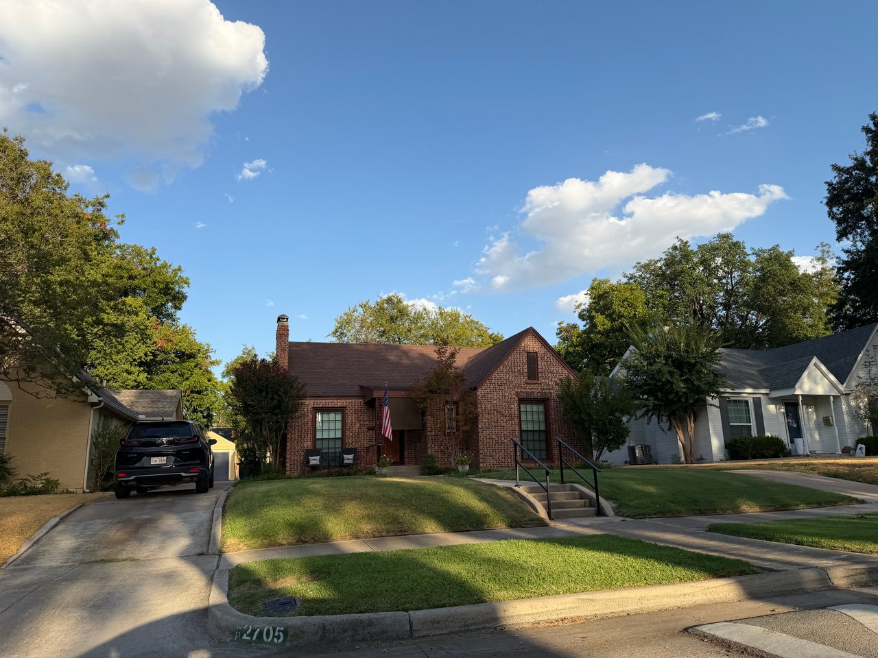 Red brick house with a front gable and entry steps, set between neighboring homes.