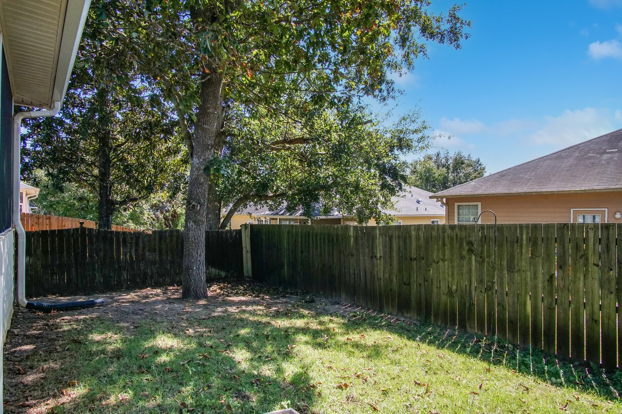 Backyard at 5441 Hampton Hill Circle, Tallahassee, Florida 32311 featuring privacy fence, grassy area, and mature shade trees.