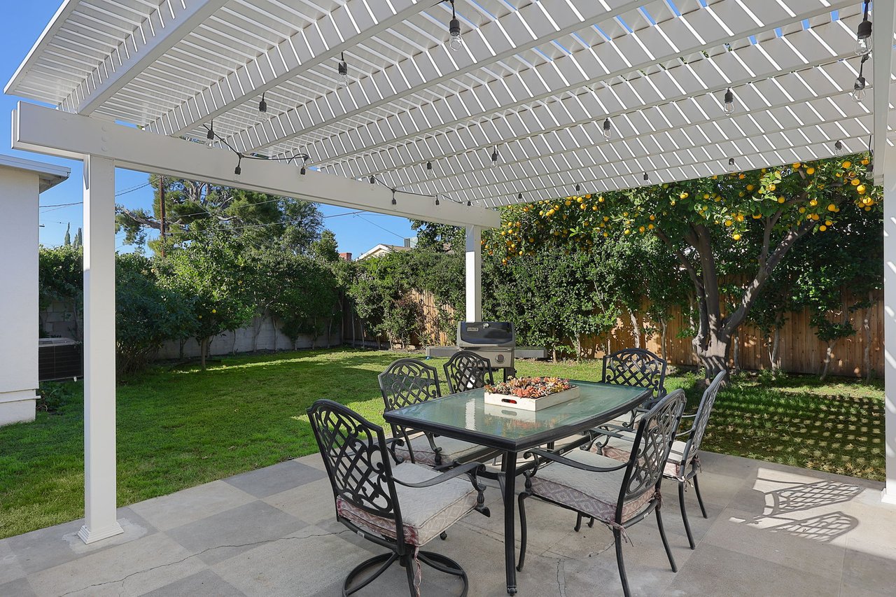 Outdoor dining area with pergola, glass-top table, and backyard views at Lake Balboa CA home